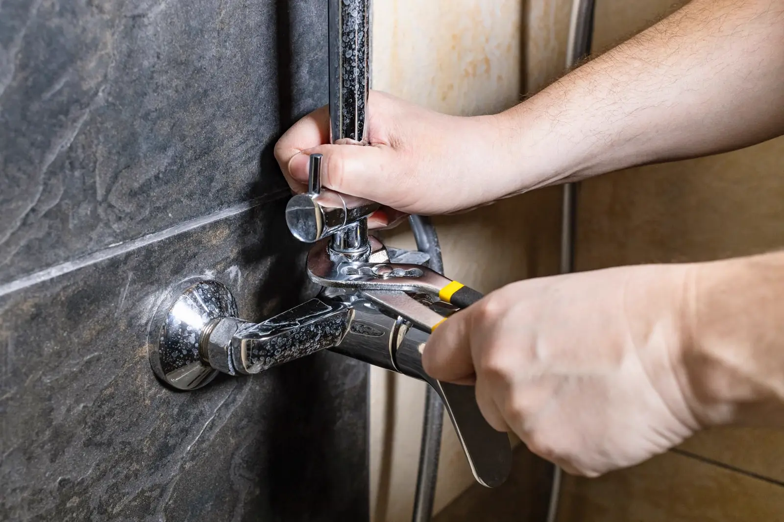 Plumber using a wrench to install a chrome shower faucet on a tiled bathroom wall